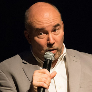 A bald man in a suit is holding a microphone
